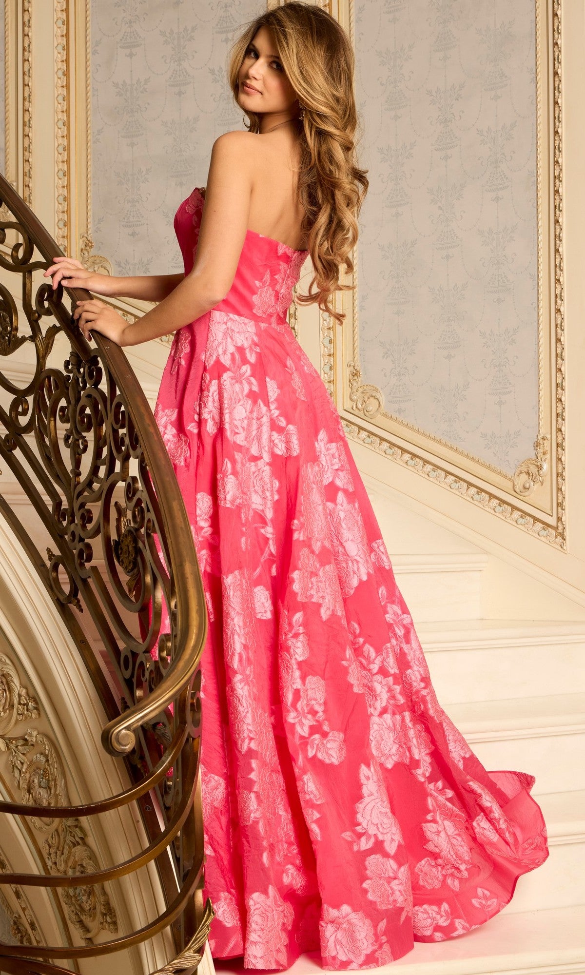 A woman wearing the Jovani 45721 long prom dress with pink floral details stands on a staircase, glancing over her shoulder at the camera.